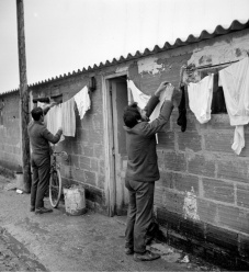 Emigrantes portugueses estendem roupa junto às barracas de um estaleiro de construção civil. Região Parisiense. 1970. Fotografia de Gerald Bloncourt.